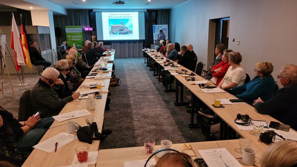 An U-förmig aufgestellten Tischen sitzen mehrere Personen und halten eine Konferenz