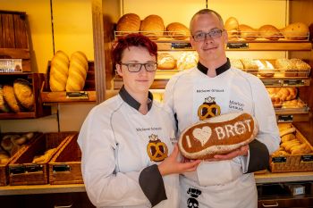 Zwei Verkäufer stehen in einer Bäckerei und halten ein Brot in den Händen