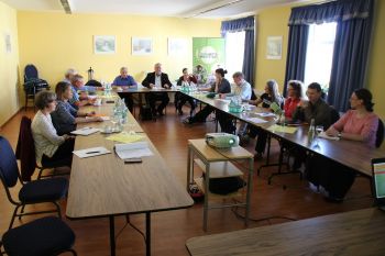 an U-förmig aufgestellten Tischen sitzen mehrere Personen und halten eine Konferenz