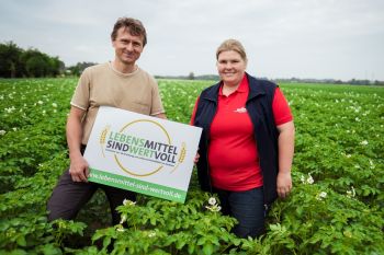 Zwei Bauens stehen in einem Kartoffelfeld, sie halten ein Schild mit der Aufschrift: Lebensmittel sind wertvoll