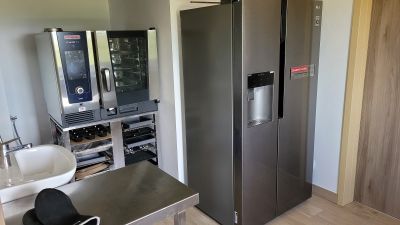 Rechts steht ein Kühlschrank, links daneben ein Ofen, darunter Backbleche und links ein Waschbecken