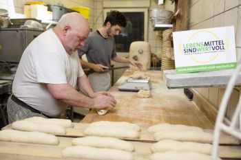 Zwei Bäckser stehen in einer Backstube und kneten Teig