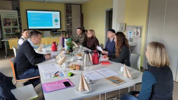 Sieben Personen sitzen an einem Tisch und beraten