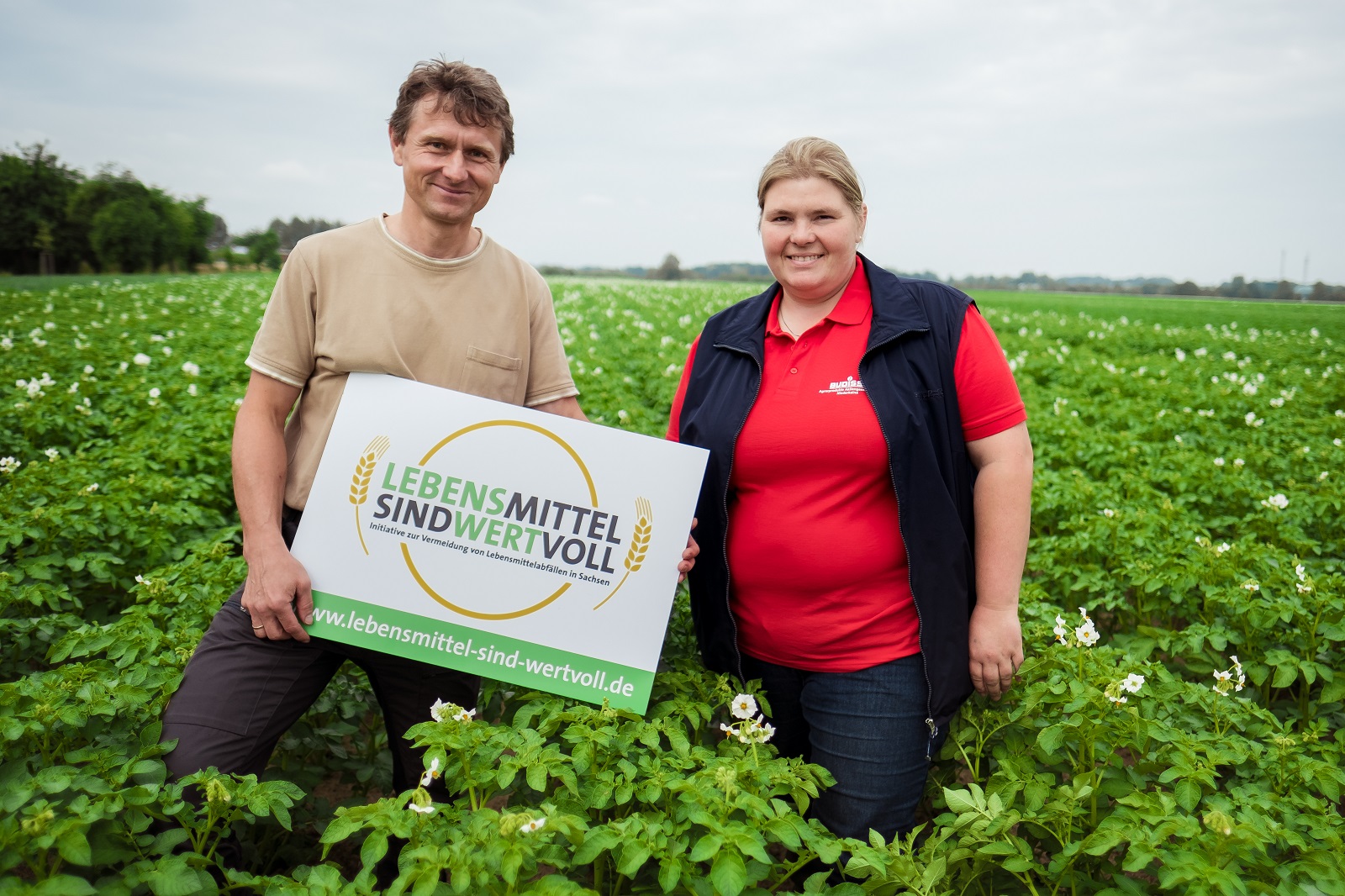 Zwei Bauens stehen in einem Kartoffelfeld, sie halten ein Schild mit der Aufschrift: Lebensmittel sind wertvoll